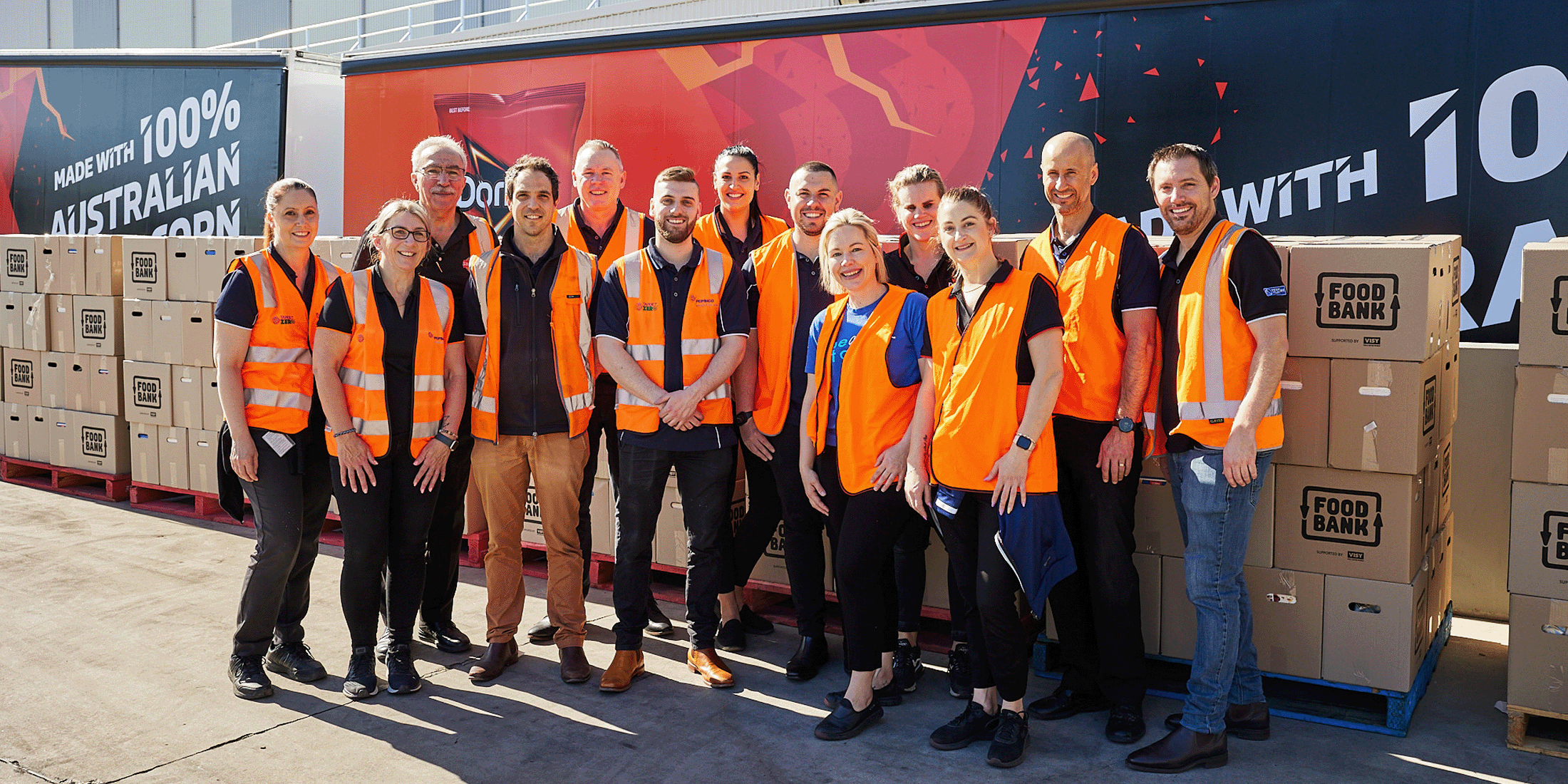 People standing together smiling next to food bank boxes